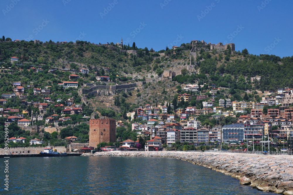 The tower of the medieval fortress stands on the sea. The fortress protects the city located on the mountain.