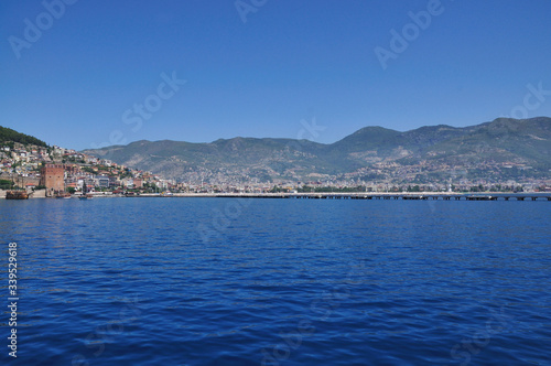 A magnificent view of the calm blue sea, the city on the mountain and the sky. Beautiful summer day on the sea shore. © Aleksandr