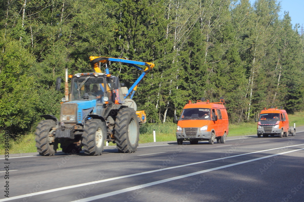 Tractor and orange special mini bus on roadside on trees background ay Sunny summer day, forest maintenance service in Russia Tractor and orange special mini bus on roadside on trees background ay Sunny summer day, forest maintenance service in Russia