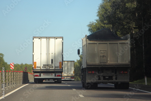 фотографія White semi truck with van trailer overtake loaded flatbed dump truck on summer c