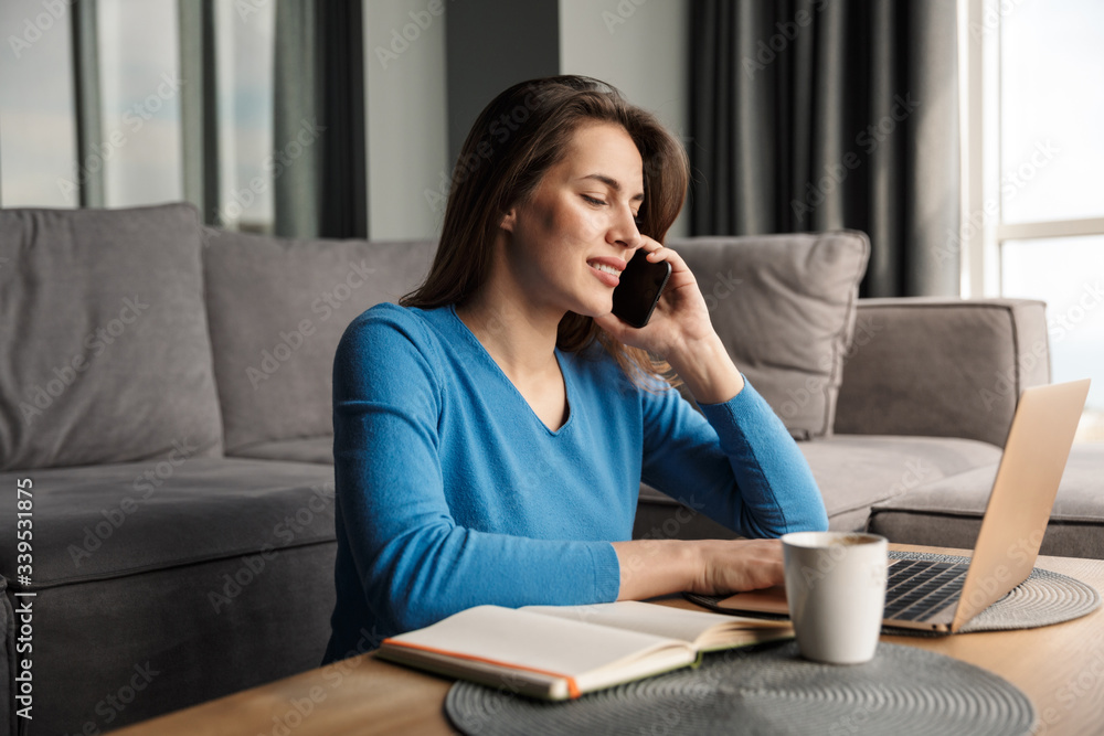 Image of smiling woman using laptop and talking on mobile phone Image of smiling woman using laptop and talking on mobile phone