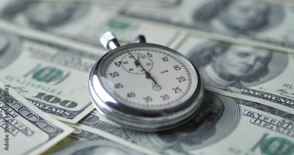 The stopwatch lies on the dollars. Time is money concept. The stopwatch lies on the dollars. Time is money concept.