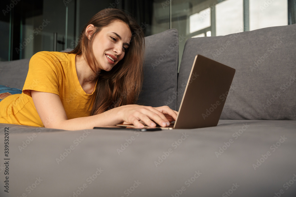 Image of smiling woman using laptop and mobile phone while lying Image of smiling woman using laptop and mobile phone while lying