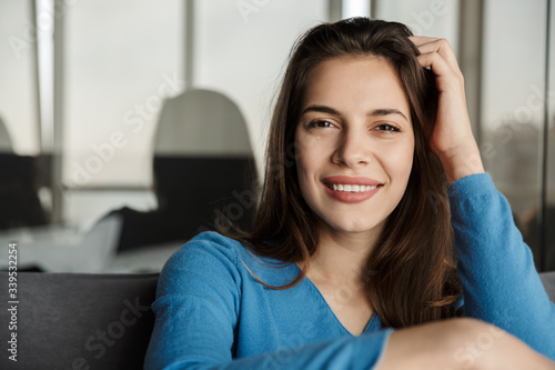Image of woman looking at camera and smiling while sitting on sofa