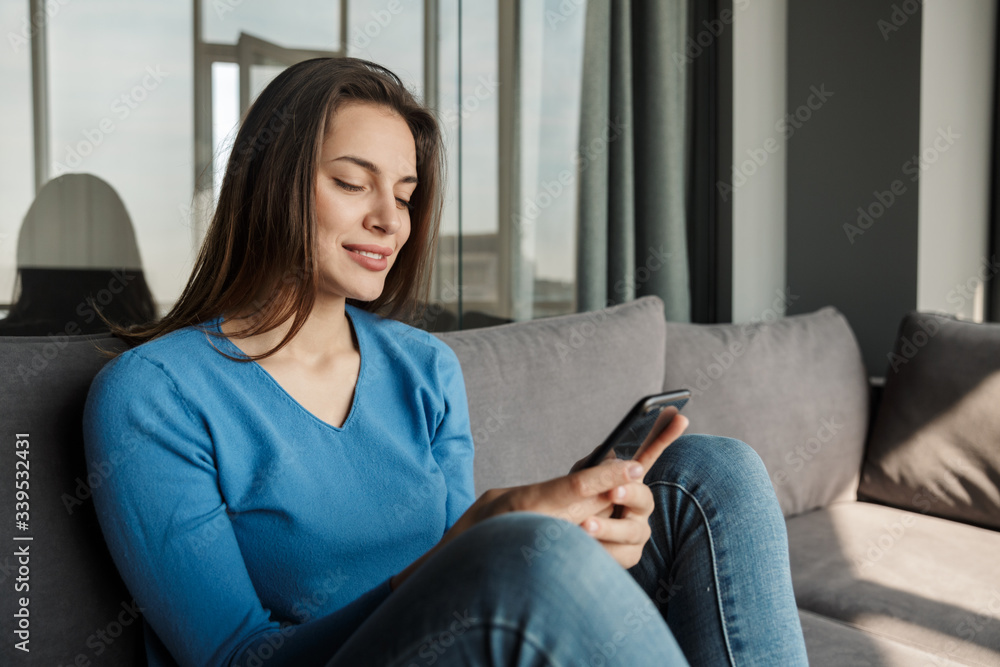 Obraz premium Image of joyful woman using cellphone and smiling while sitting on sofa