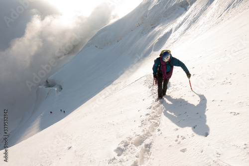 A climber ascending a steep glacier slope with sunrise light in Ecrins, French Alps.