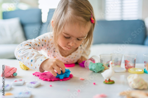 Happy little child, adorable creative 2 year old girl playing with dough, colorful modeling compound, sitting bright sunny room at home.