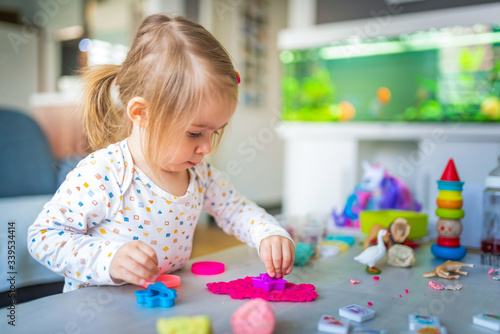 Happy little child, adorable creative 2 year old girl playing with dough, colorful modeling compound, sitting bright sunny room at home.