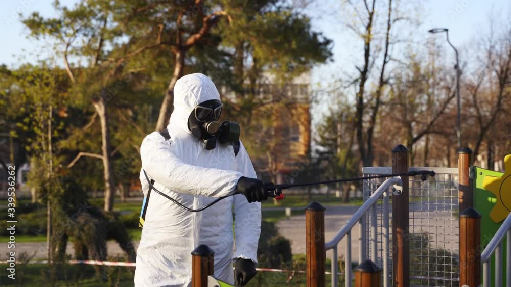 Hazmat team disinfects playground surfaces on coronavirus covid-19 quarantine with antibacterial sanitizer sprayer. Worker in gas mask and protective suit decontaminates children rides, slide, street. Hazmat team disinfects playground surfaces on coronavirus covid-19 quarantine with antibacterial sanitizer sprayer. Worker in gas mask and protective suit decontaminates children rides, slide, street.