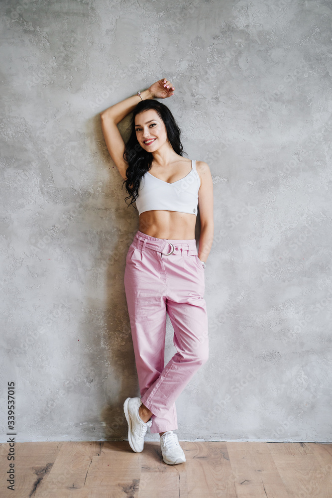 Portrait of fashionable young brunette woman dressed in pink pants, sneakers