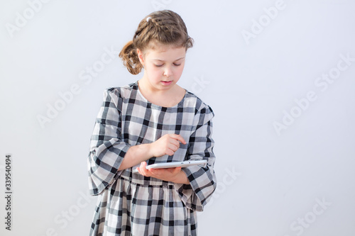 Caucasian little girl stands with mobile white digital tablet on white background and searches for the right information, web page. Digital Technology Learning Concept for School Child Lifestyle