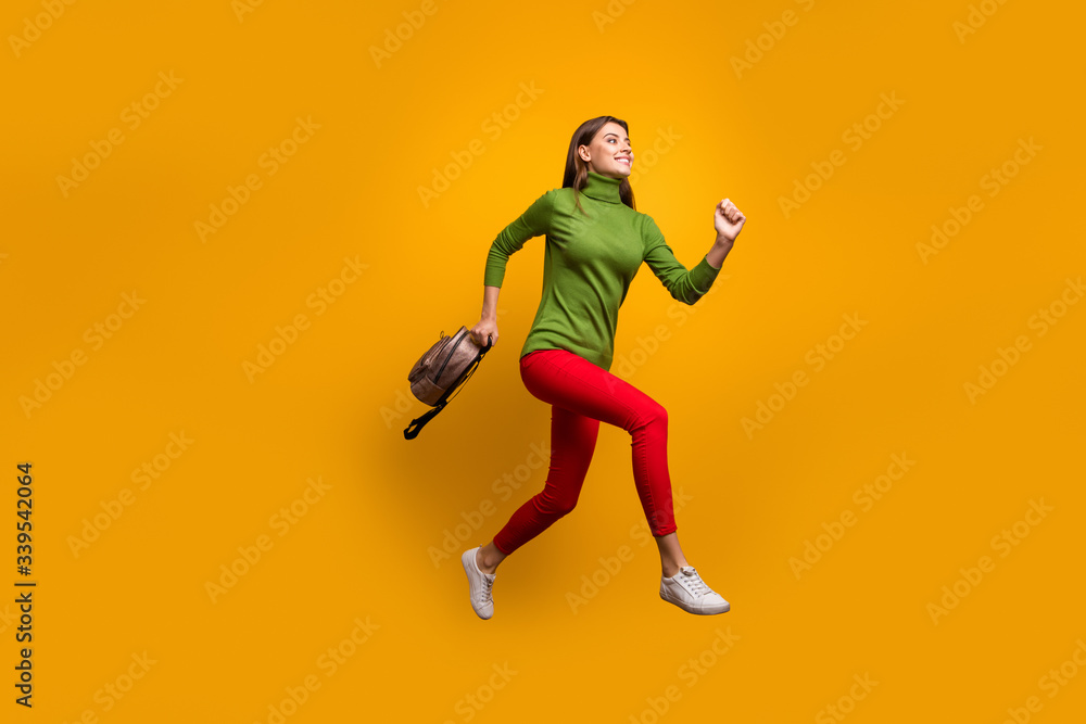 Full body profile photo of funky pretty lady jumping high holding cool youngster bag rushing home after studying wear casual green jumper red pants isolated yellow color background
