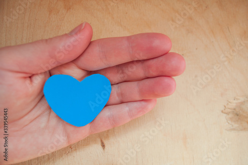 Hand holds a blue heart. Symbol of trust, platonic love, fidelity, loyalty and friendship. Supporting the appearance of autism. Love of water sports.