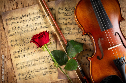 Tela classic retro violin music string instrumt on old music note sheet paper with red rose flower old oak wood wooden background