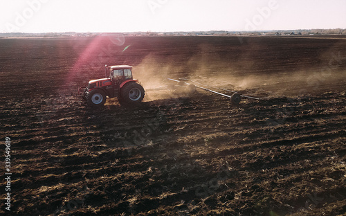 Farm tractor raising dust with harrow plow preparing land for sowing. Agriculture industry, cultivation of land.
