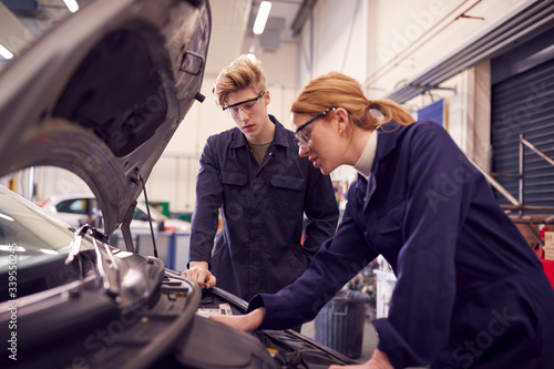 Male And Female Students Looking At Car Engine On Auto Mechanic Apprenticeship Course At College