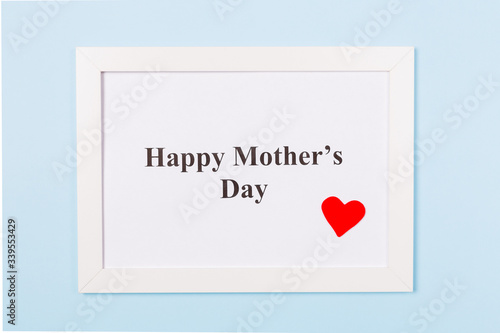 White picture frame with text Happy Mother's Day and red heart on light blue background . Happy Mother's Day concept.