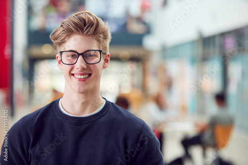 Portrait Of Smiling Male College Student In Busy Communal Campus Building