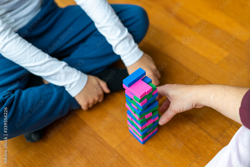Close up of mother and son playing colorful wooden blocks stack tower game for children on the floor of the house sharing time together at home