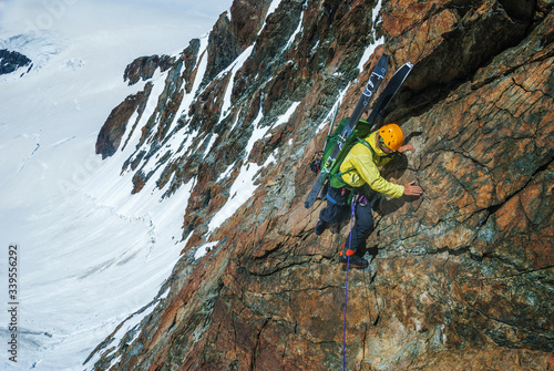 Climber with skis on a steep cliff above the glacier.