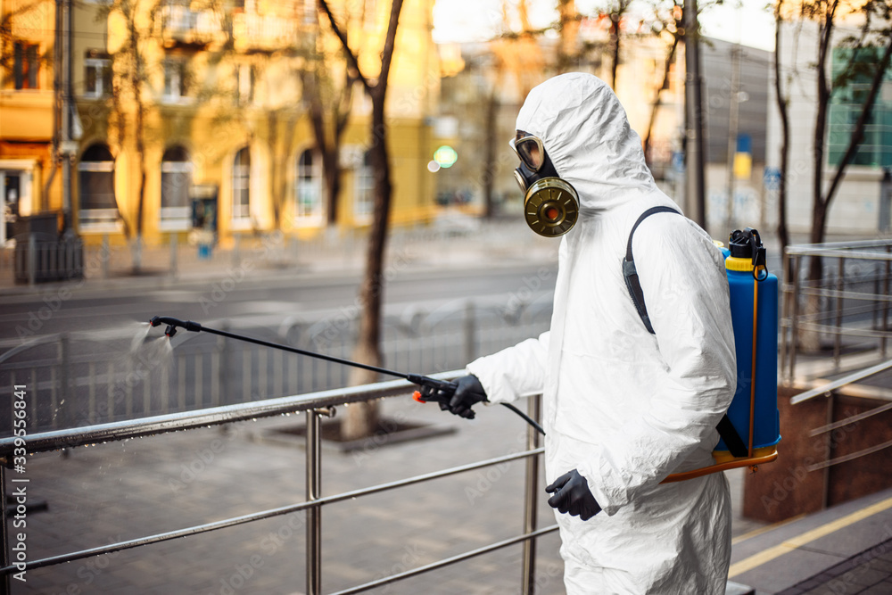 Man sprays disinfector onto the railing wearing coronavirus protective suit and equipment. Cleaning and sterilizing the not crowded city streets. Covid-19 nCov2019 spread prevention. Man sprays disinfector onto the railing wearing coronavirus protective suit and equipment. Cleaning and sterilizing the not crowded city streets. Covid-19 nCov2019 spread prevention.