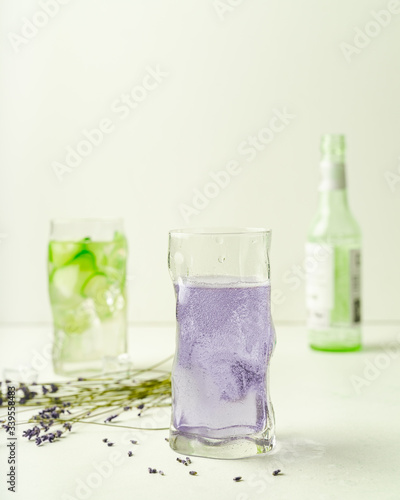 Two glasses of summer refreshing drinks, lavender lemonade and cucumber infused water, and empty bottle