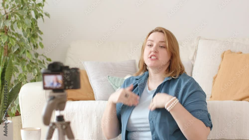A Young Female Vlogger Recording a Video for an Online Blog with Camera on Tripod. The Blogger Talks and Gestures. Cozy White Home Interior with House Plants. Concept of Video Blogging. A Young Female Vlogger Recording a Video for an Online Blog with Camera on Tripod. The Blogger Talks and Gestures. Cozy White Home Interior with House Plants. Concept of Video Blogging.