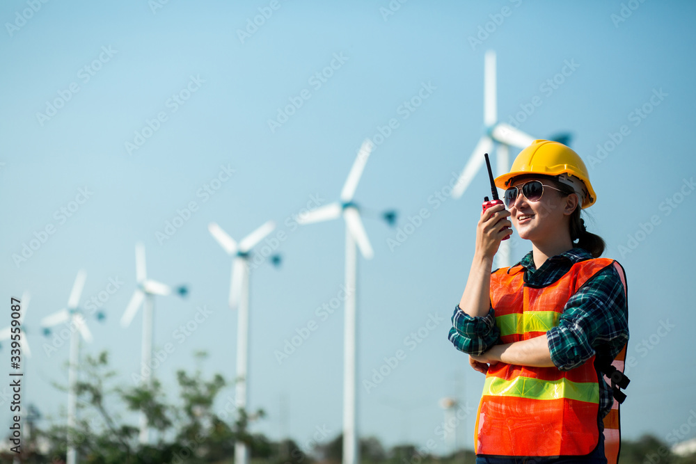 Young engineer woman holding a walkie talkie to check wind turbine system, concept of renewable energy Young engineer woman holding a walkie talkie to check wind turbine system, concept of renewable energy
