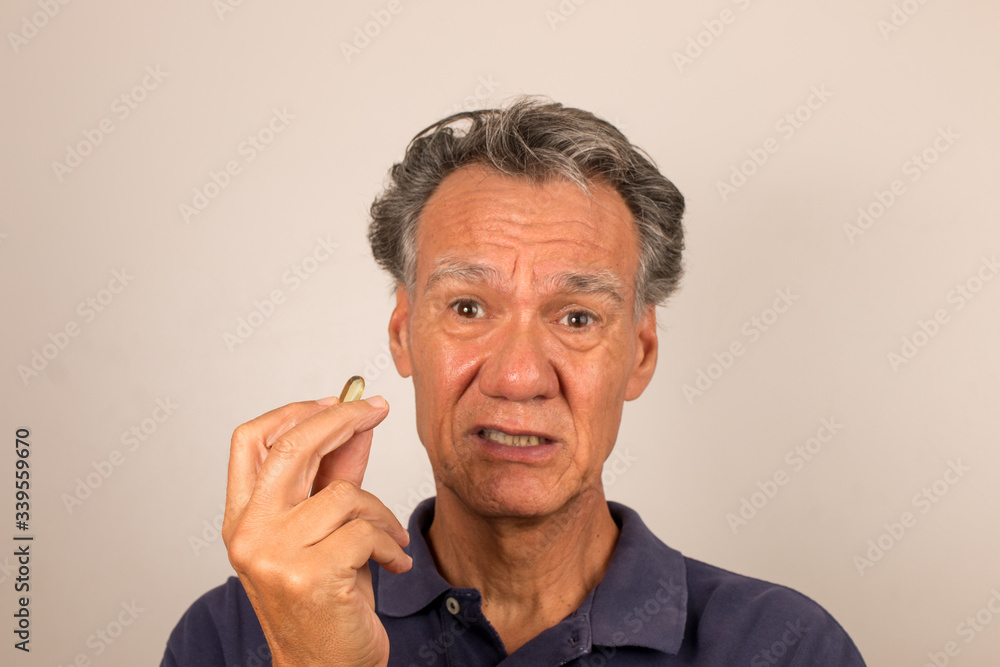 Senior Man Holding Vitamins/Medication in his hand contemplating whether to take them Senior Man Holding Vitamins/Medication in his hand contemplating whether to take them