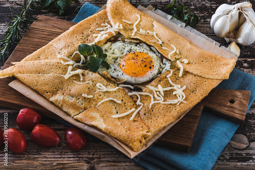 Photos French pancake with fried egg, herbes and cheese on a wooden slat