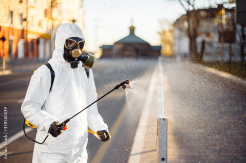 Disinfection team worker is cleaning pavement fence with a sterilizing water spraying it over the coronavirus infected surface. Covid-19 protective equipment and actions to stop spread of the disease. © Konstantin Zibert