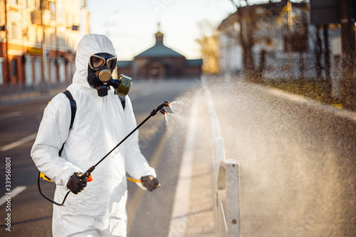 Disinfection team worker is cleaning pavement fence with a sterilizing water spraying it over the coronavirus infected surface. Covid-19 protective equipment and actions to stop spread of the disease. photo