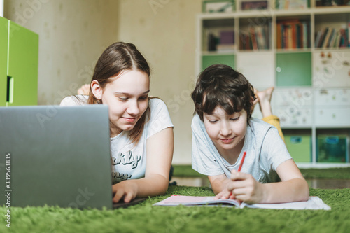 Siblings brother sister attractive girl teenager and tween boy do homework learn foreign language writing in pupil book with opened laptop at the room home dictance education photo