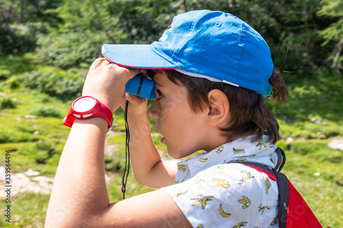 child looks through spyglass binoculars at nature during a mountain hike in summer