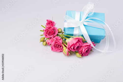 Blue gift box with white ribbon bow and bouquet of red roses on white background