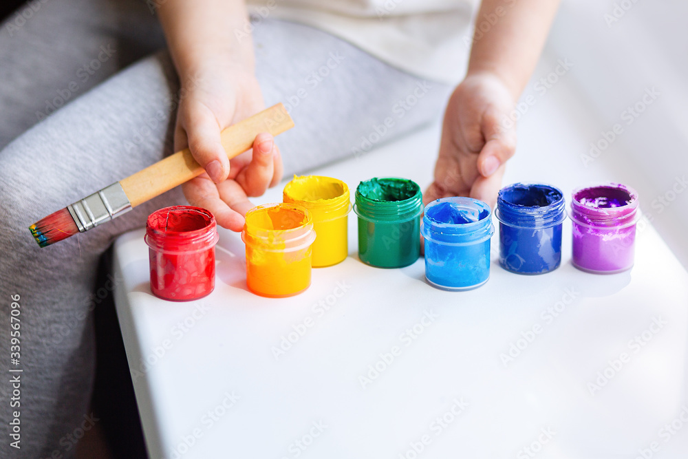 Paint the colors of the rainbow. Children's hands with a brush and paints. The child holds colorful paint for drawing. Paint the colors of the rainbow. Children's hands with a brush and paints. The child holds colorful paint for drawing.