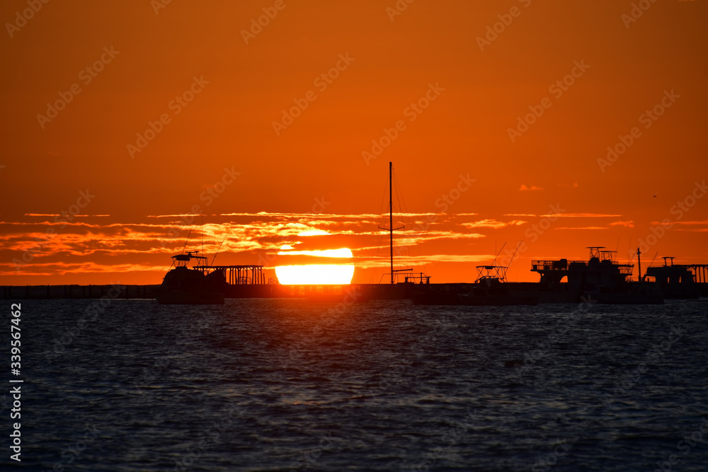 Orange sun rising from the horizon at dawn against the background of silhouettes of fishing boats