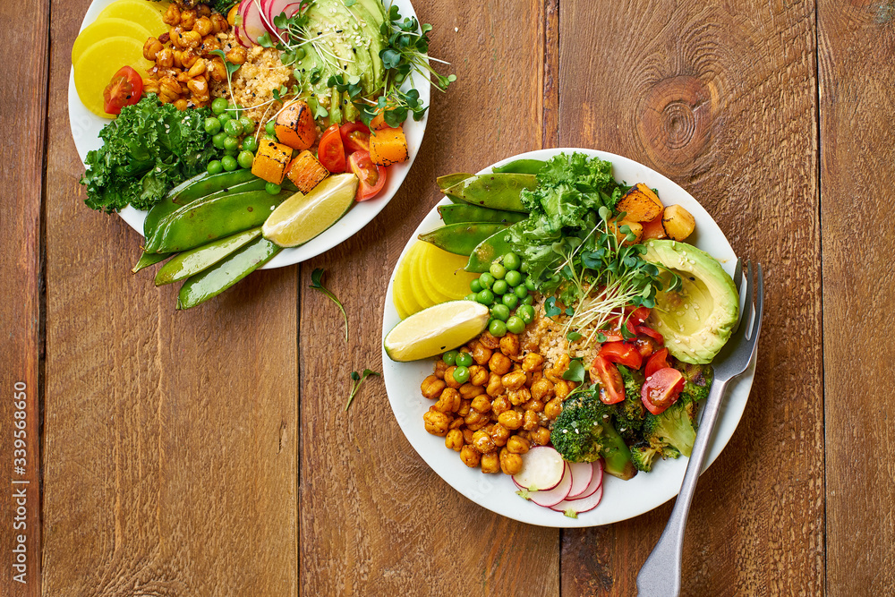 Healthy vegetarian lunch bowl with avocado, chickpeas, quinoa and vegetables, garnished with microgreens and nut dressing. Flat lay on wooden background. Healthy vegetarian lunch bowl with avocado, chickpeas, quinoa and vegetables, garnished with microgreens and nut dressing. Flat lay on wooden background.