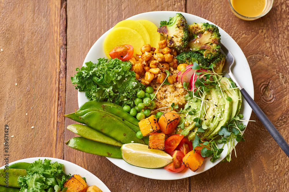 Overhead shot of healthy vegetarian lunch bowl with avocado, chickpeas, quinoa and vegetables, garnished with microgreens and nut dressing. Flat lay on wooden background. Overhead shot of healthy vegetarian lunch bowl with avocado, chickpeas, quinoa and vegetables, garnished with microgreens and nut dressing. Flat lay on wooden background.