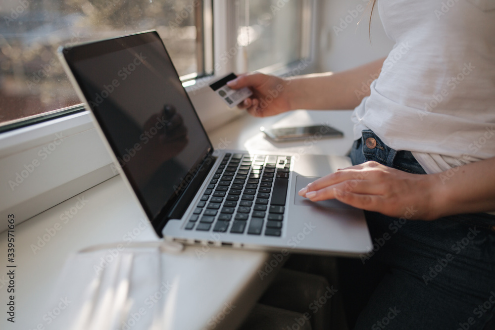 Close up of young woman shopping online using laptop phone and credit card. Laptop on windowsill Close up of young woman shopping online using laptop phone and credit card. Laptop on windowsill