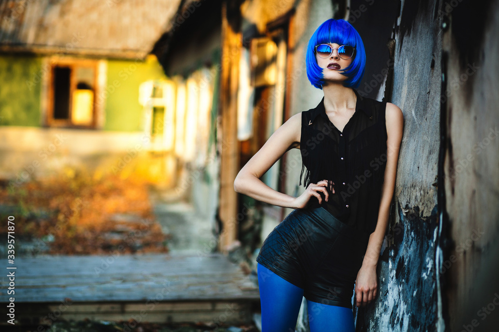 Woman with short electric blue hair and sunglasses posing on urban wall background. Concept of future and cosmos. 
