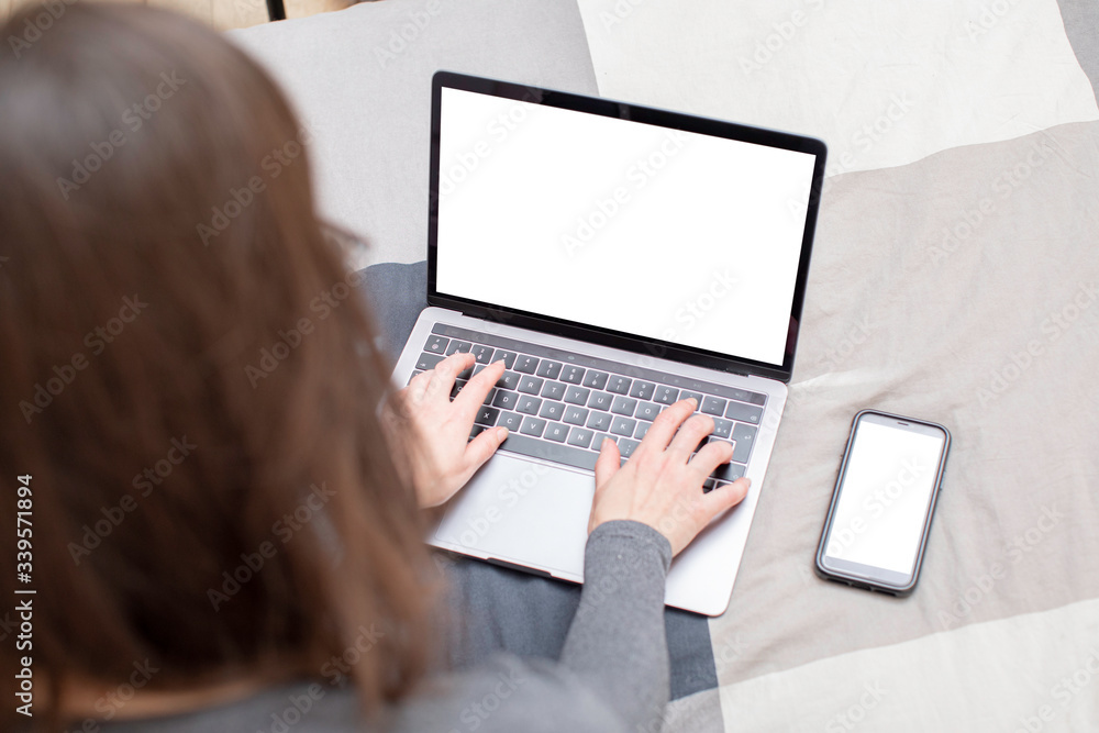 Young woman surfing on her metallic gray laptop and looking for informations on the internet. She has long brown hair, glasses and a gray sweater, and she sits on a plaid patterned sheet Young woman surfing on her metallic gray laptop and looking for informations on the internet. She has long brown hair, glasses and a gray sweater, and she sits on a plaid patterned sheet