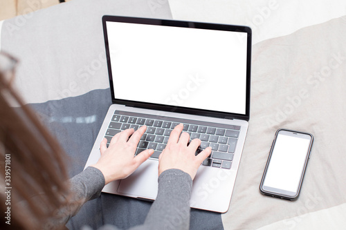 Young woman surfing on her metallic gray laptop and looking for informations on the internet. She has long brown hair, glasses and a gray sweater,  and she sits on a plaid patterned sheet