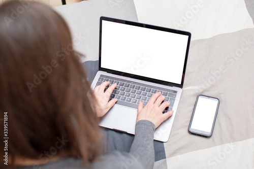 Young woman surfing on her metallic gray laptop and looking for informations on the internet. She has long brown hair, glasses and a gray sweater, and she sits on a plaid patterned sheet