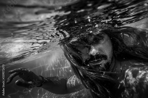Artistic pic out of focus underwater with long hair man swimming with bubble in water, dark underwater atmosphere with nightmare human abyssal creature like mermaid with beard photo