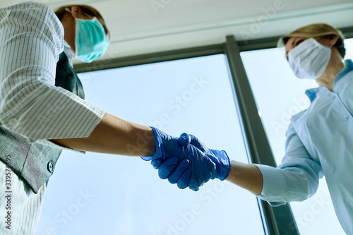 Below view of businesswomen shaking hands while wearing protective gloves.