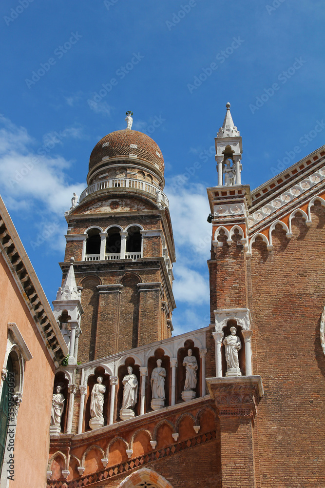 Detail of the facade and bell tower of the church of the Madonna dell'Orto in Venice. The building is in Venetian Gothic style, made of brick with decorative elements in stone and marble. Italy.