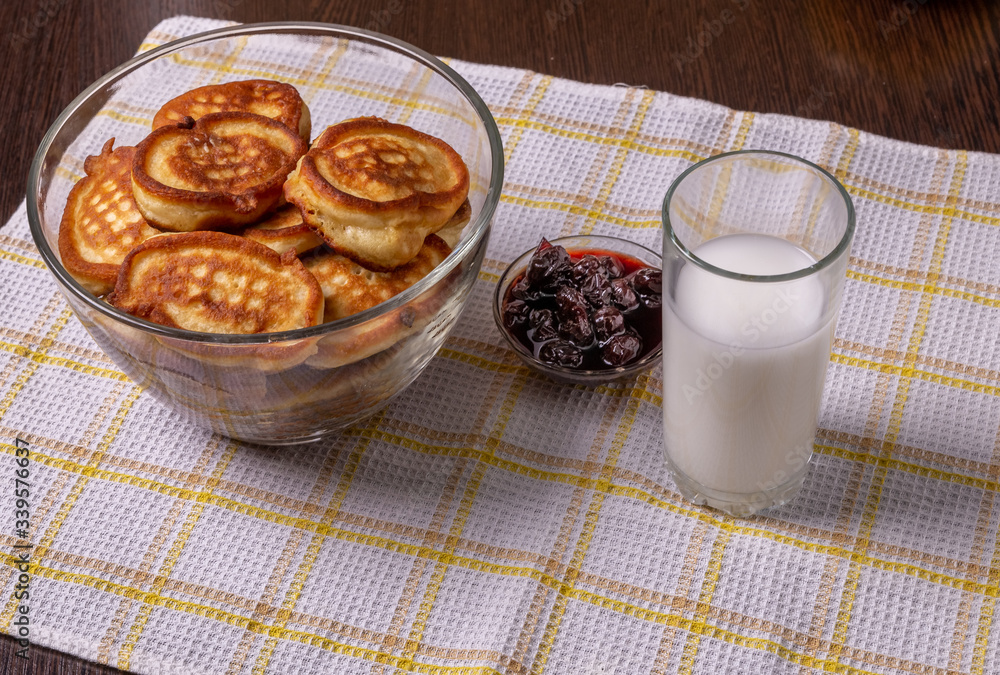 Pancakes on a plate, milk in a glass, and jam on a napkin on the table. Pancakes on a plate, milk in a glass, and jam on a napkin on the table.