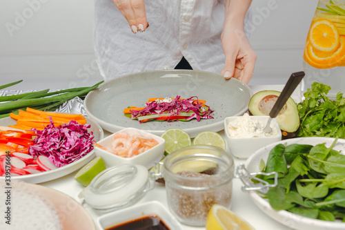Fototapeta Naklejka Na Ścianę i Meble -  Woman's hands adding seeds to spring roll with red cabbage, cheese, carrots, cucumbers. Table with spring rolls ingredients, organic and fresh vegetables.