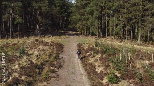 Drone footage of a person mountain biking along an empty country track heading towards a forest on a sunny morning in North Yorkshire England completely isolated photo